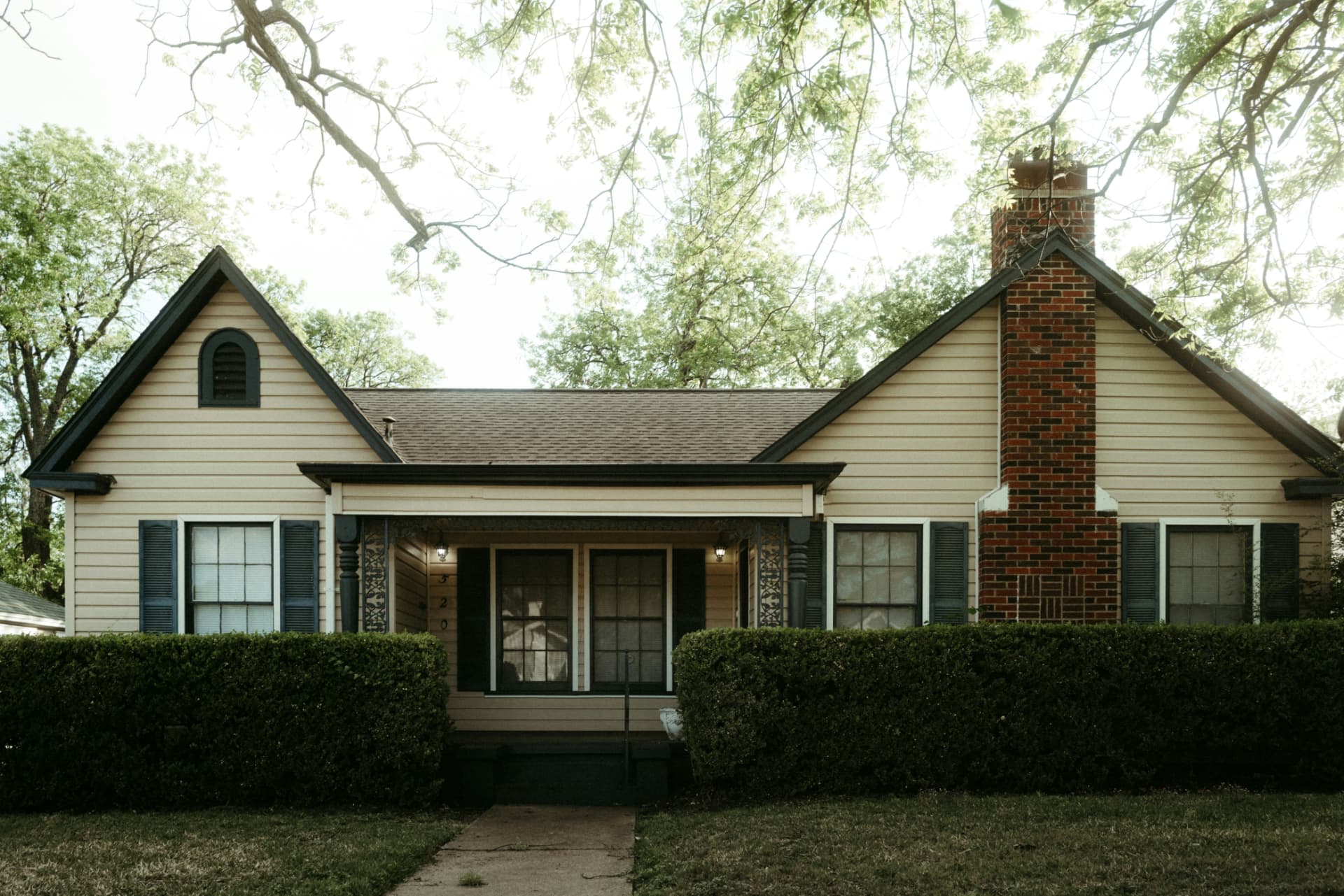 Cottage-style home with a brick chimney on a shaded street