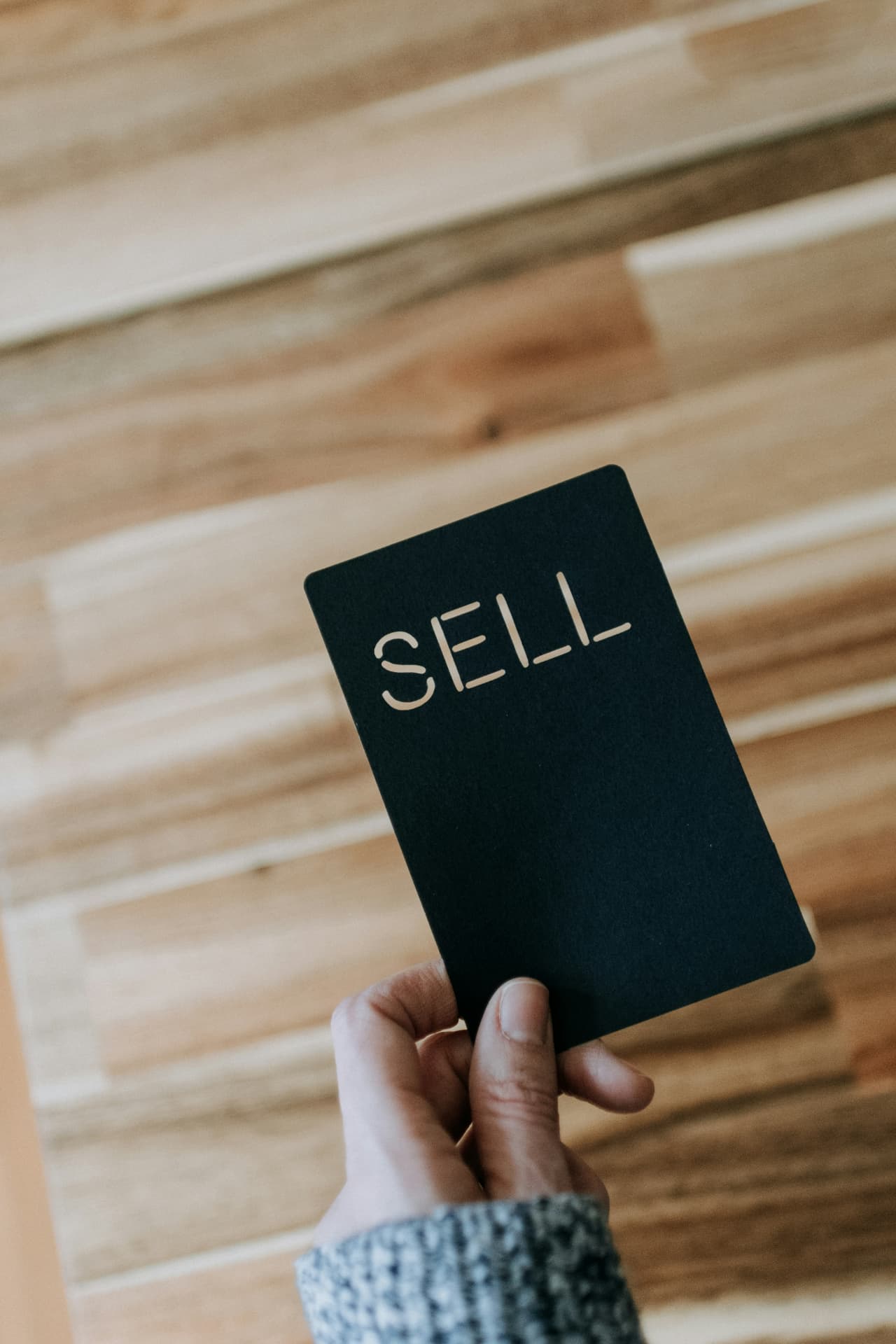 A hand holding a card that reads SELL